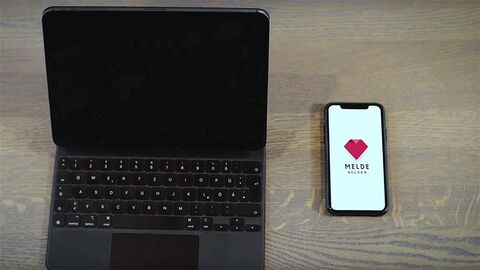 Laptop mit schwarzem Bildschirm und Smartphone mit dem Logo von MeldeHelden