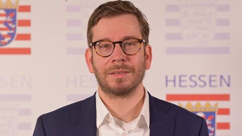 Portrait Michael Achtert vor einer Wand mit mehreren Hessenmarken.